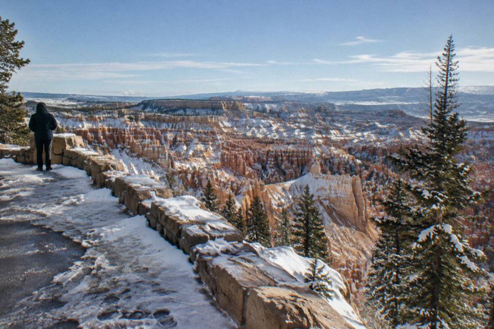 A snow-dusted rim overlook with red rock hoodoo columns below under a clear sky