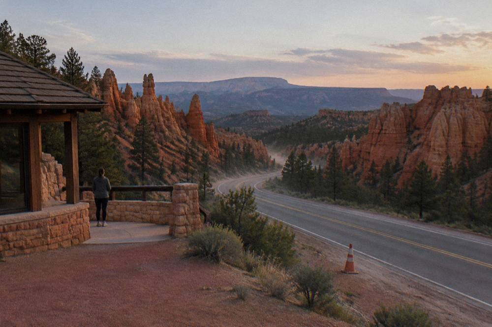 A winding two-lane road cutting through red rock cliffs toward distant canyon mesas