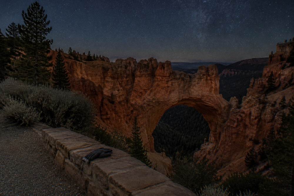 A dark night sky filled with stars above the silhouetted edge of a canyon plateau