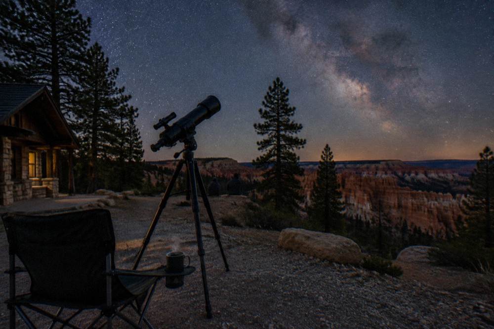Telescope silhouetted against a star-filled sky above dark pines
