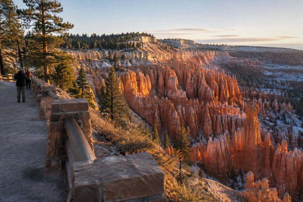 Golden morning light on tall orange rock spires below a pine-dotted rim