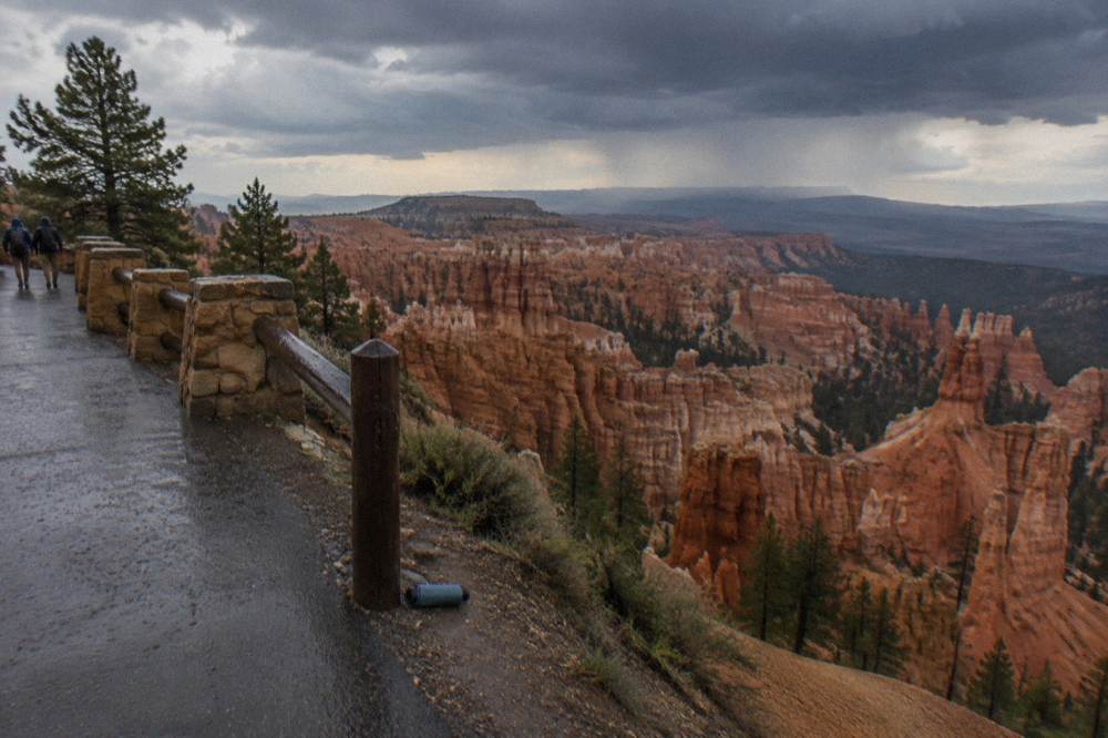 Paved path along the rim with hoodoo formations and distant plateau visible below