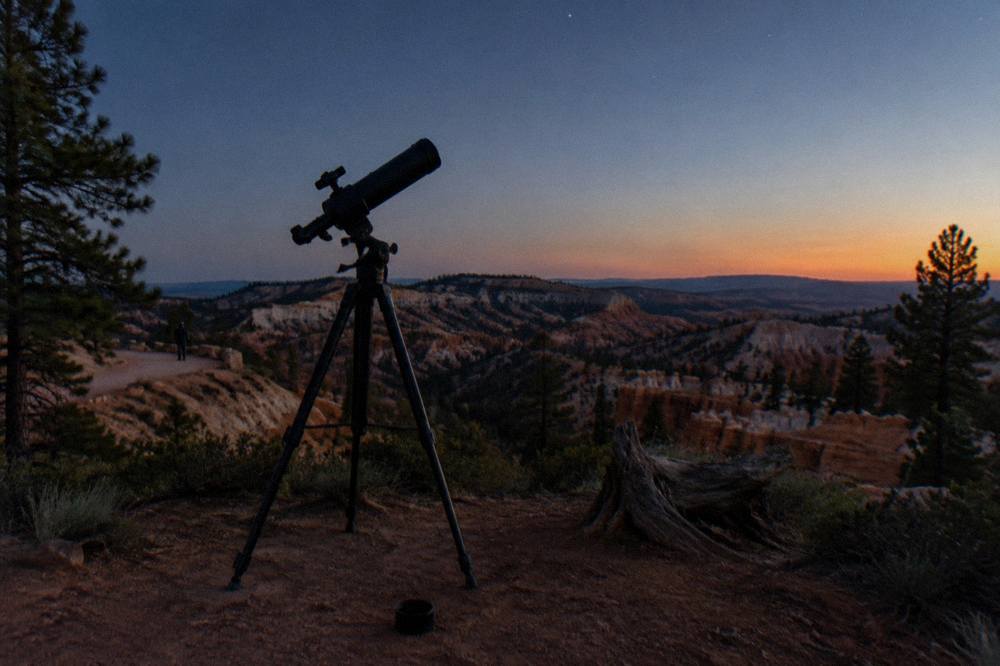 Telescope silhouetted against a starry sky above a desert plateau at dusk