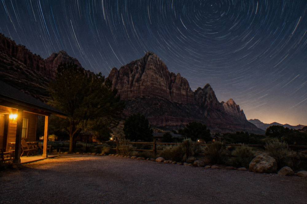 Star trails over dark canyon cliffs with a small glow on the horizon