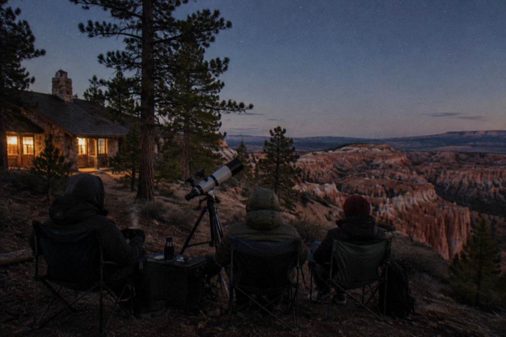 People in chairs around a telescope on a dark plateau under the Milky Way