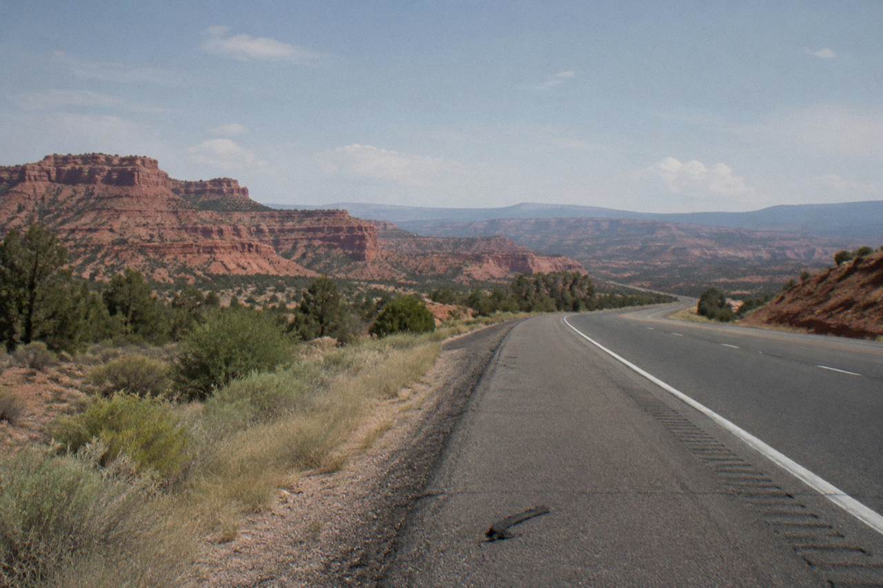 Red rock cliffs and open desert highway stretching toward distant canyon mesas under a wide sky