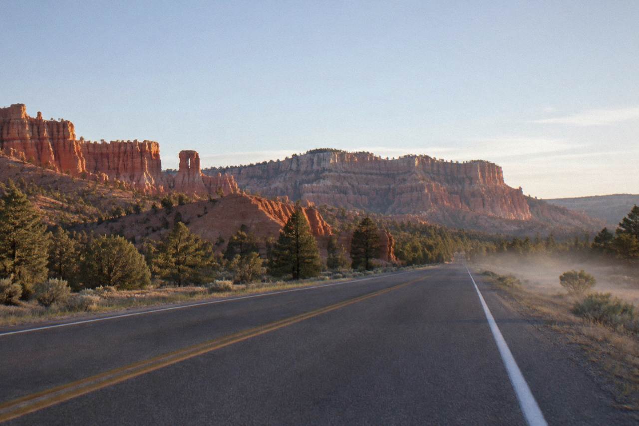 Empty desert highway running toward red rock cliffs under a wide sky