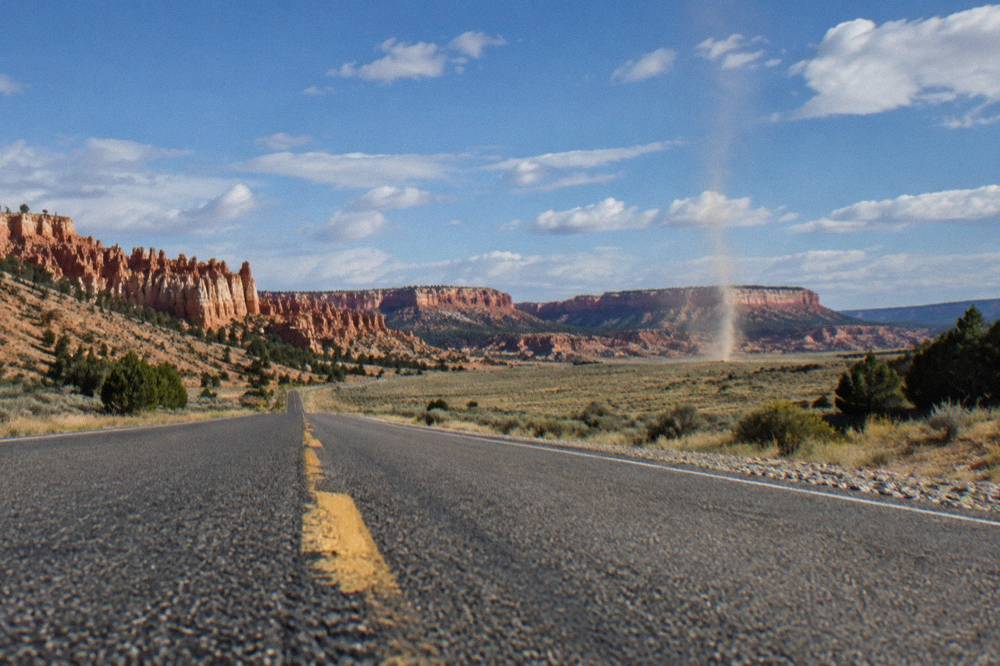 An empty highway stretching toward distant red cliffs and mesa formations