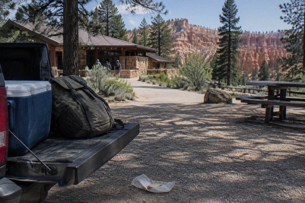 Cooler and backpack on a tailgate beside pine forest at a Bryce Canyon picnic area