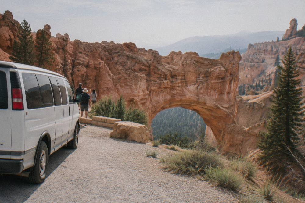 A guided tour miniban parked at a Bryce Canyon overlook with rows of orange hoodoos below