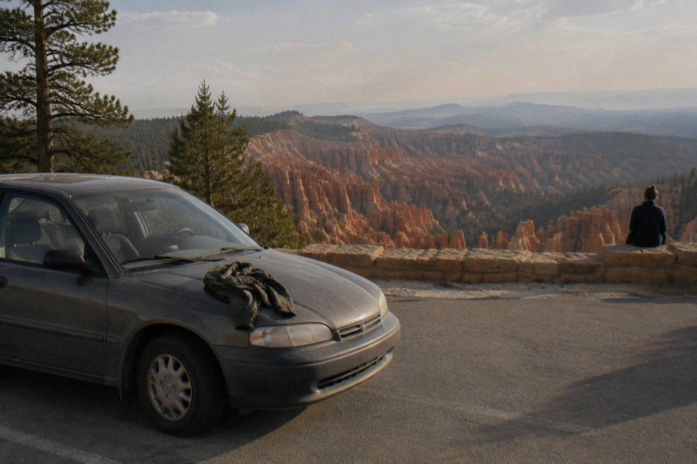 A car parked at an empty Bryce Canyon overlook with hoodoo spires below under an afternoon sky