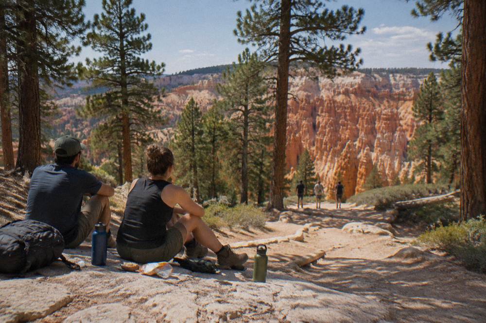Hikers resting with water bottles and snacks on a rocky trail among tall pine trees