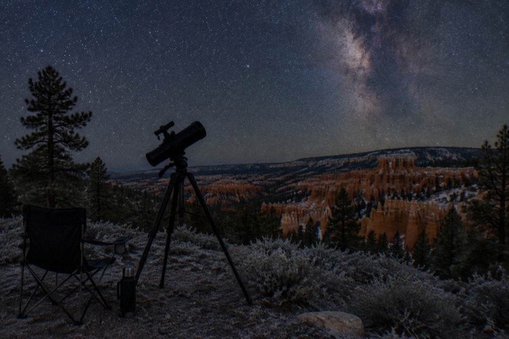 Telescope silhouetted against a star-filled night sky over dark plateaus