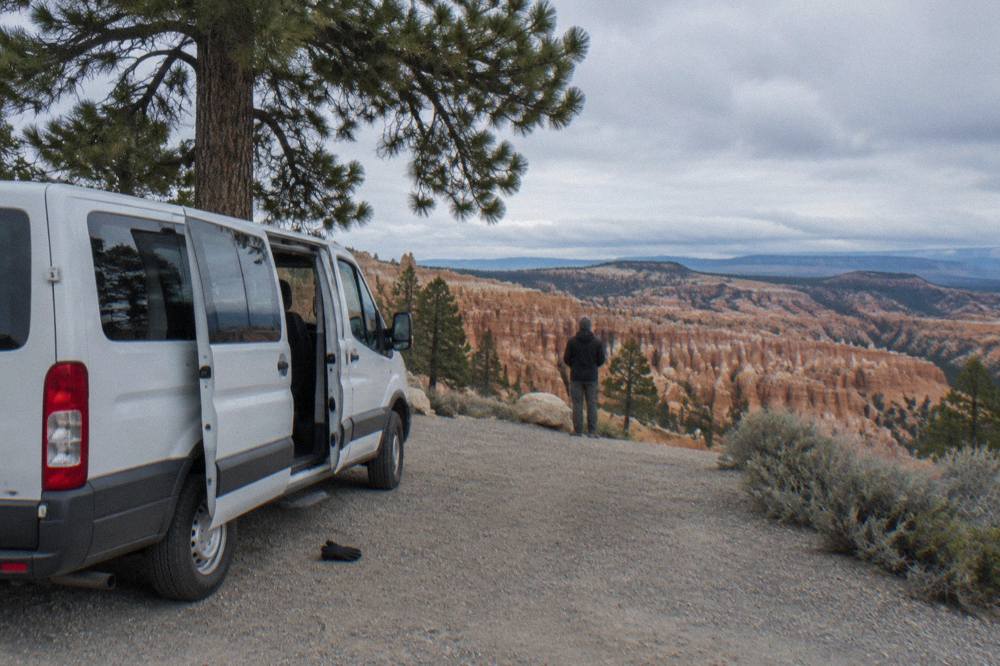 A guided tour minivan parked at an overlook above eroded orange rock formations