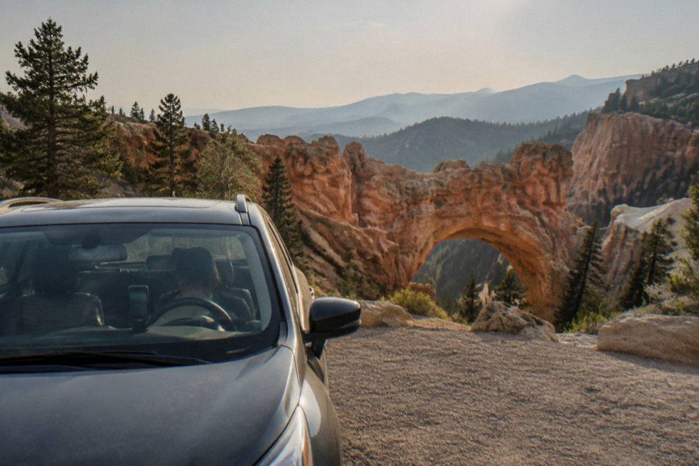 A car parked at an empty overlook above a wide canyon of rock spires