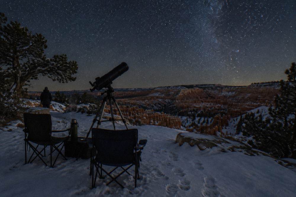 Telescope silhouetted against a star-filled night sky above a snowy plateau