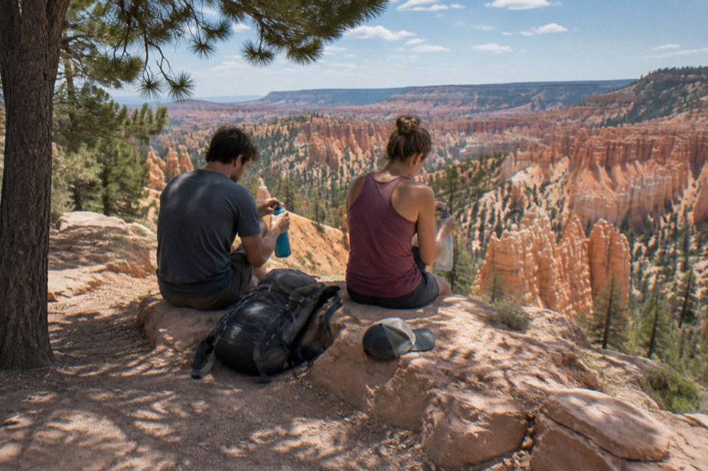 Hikers resting with water bottles at a shaded viewpoint above eroded rock spires