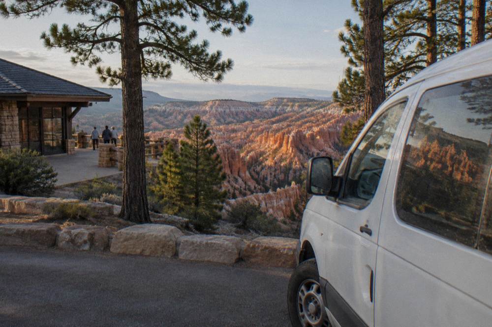 Tour van parked at a Bryce Canyon overlook with pine trees and hoodoos beyond