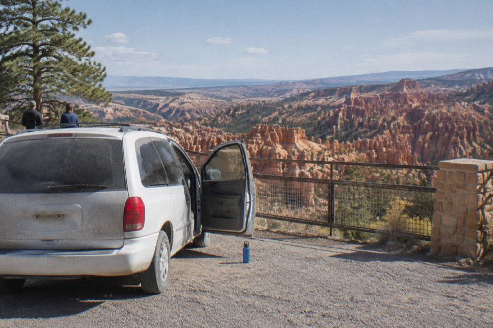 A minivan parked at a Bryce Canyon overlook with hoodoos beyond the railing