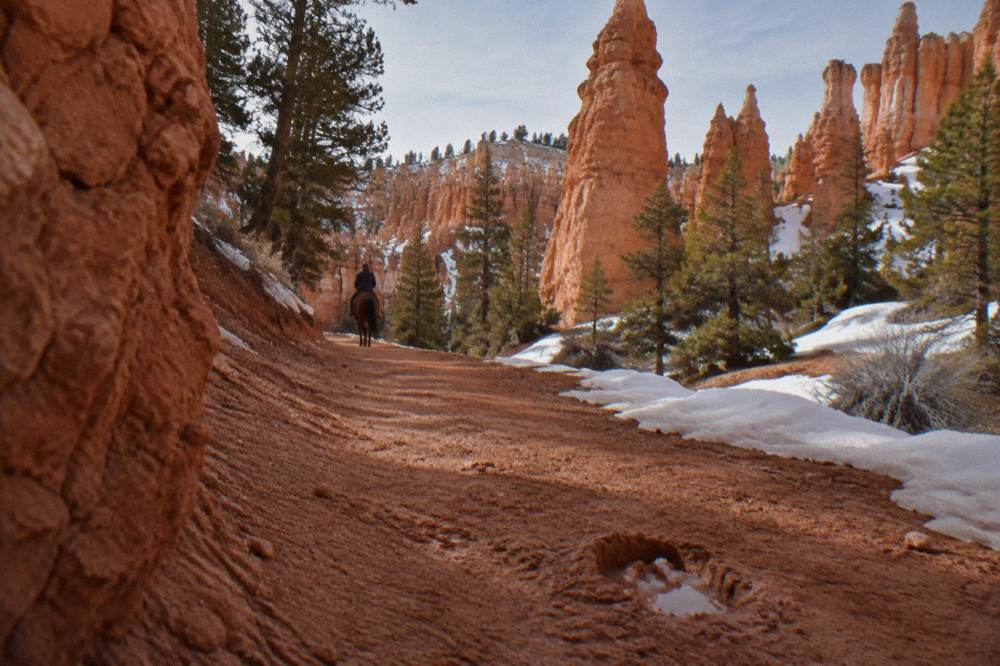 A riding trail winding through red rock formations with patchy snow on the ground