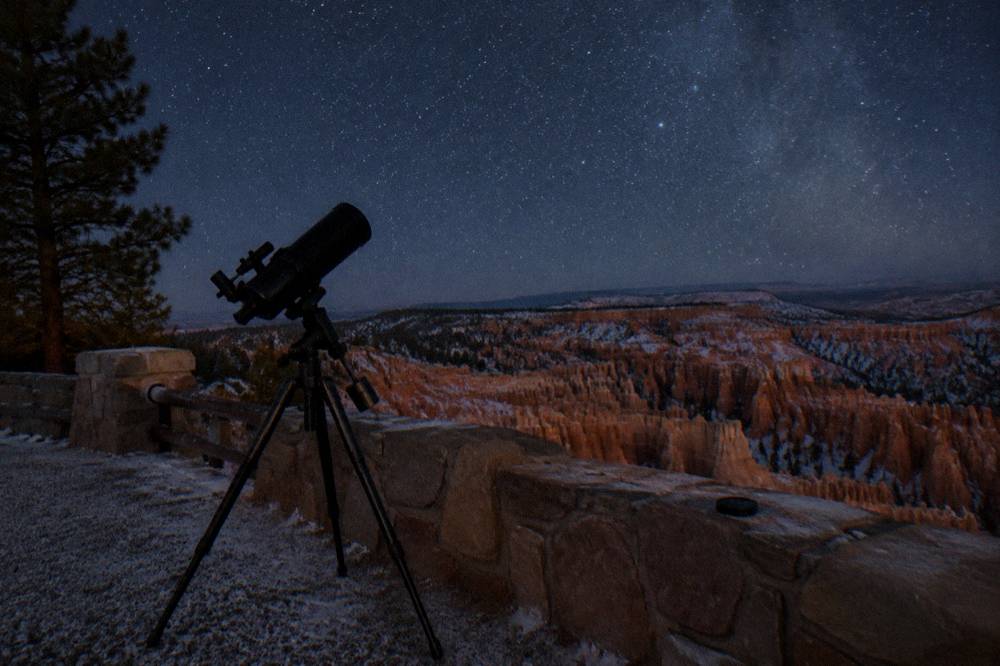 Telescope silhouetted against a star filled night sky above red rock terrain