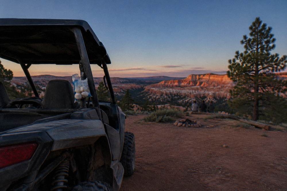 An open-air UTV parked at dusk facing a horizon of red rock cliffs under a deep blue sky