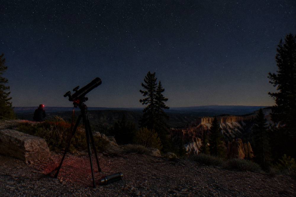 A telescope silhouetted against a star-filled night sky above dark desert hills