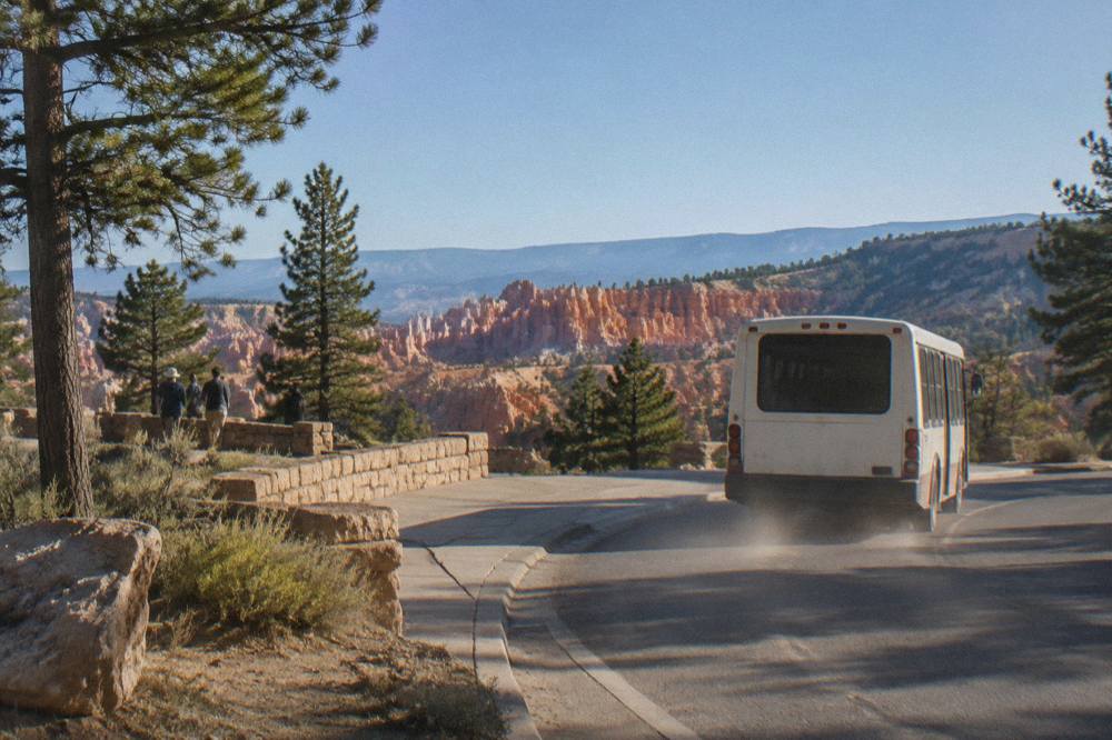 A shuttle bus pulling away from a curb beside pine trees at Bryce Canyon
