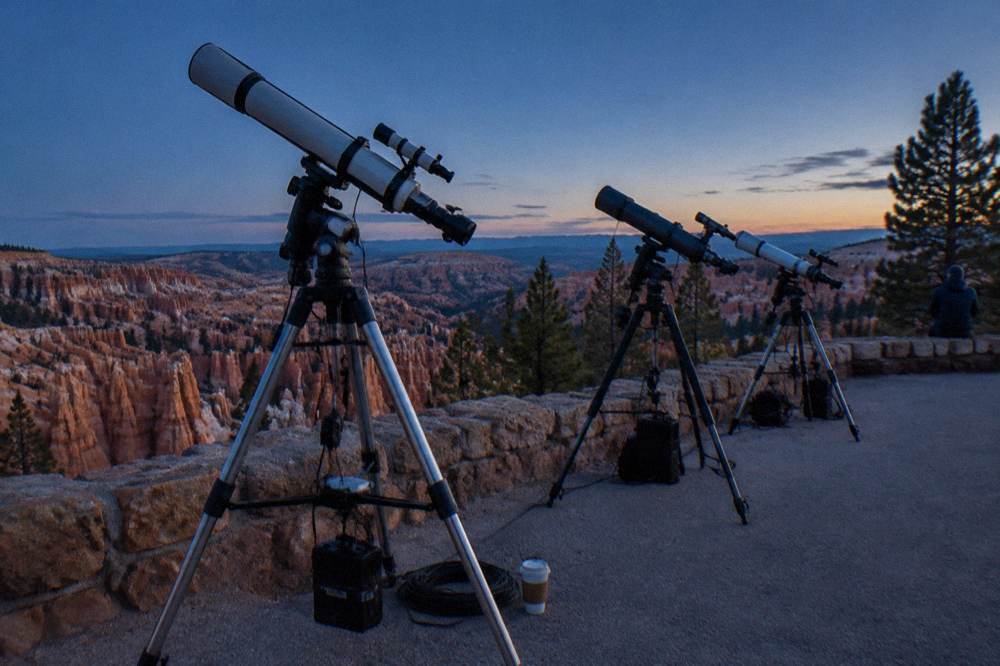 Astronomy telescopes lined up on a paved overlook at dusk