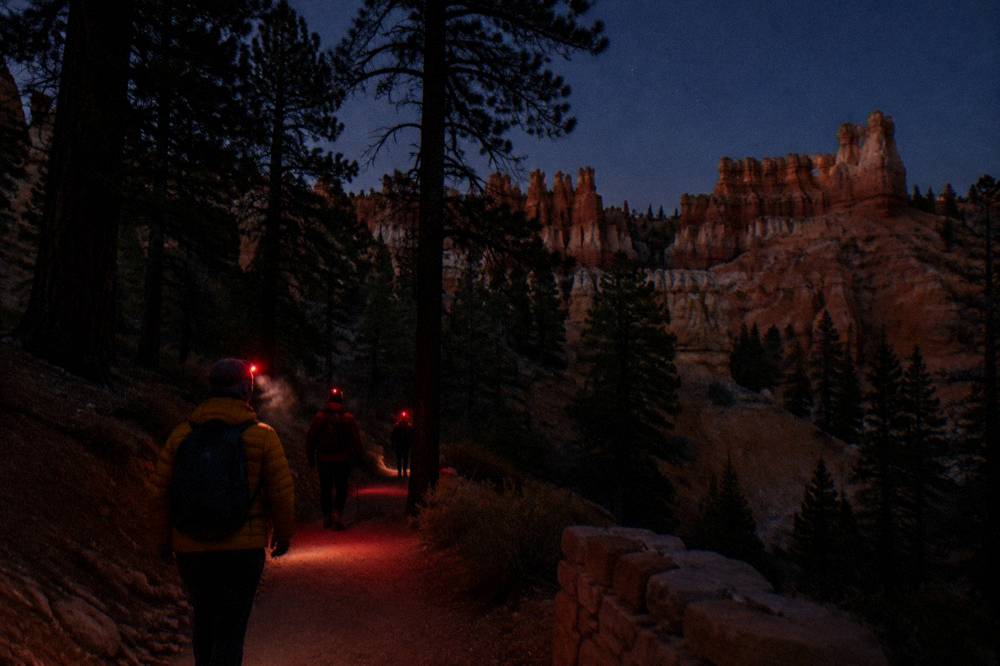Red headlamp glow and warm jackets on a dark plateau pathway