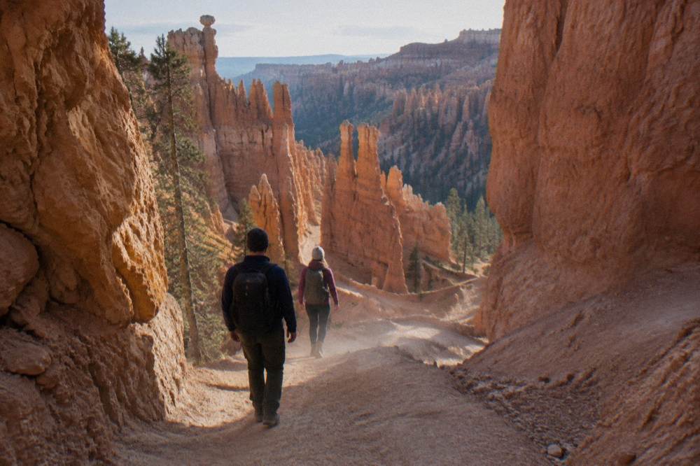 Hikers descending a switchback trail between tall orange hoodoo walls in Bryce Amphitheater