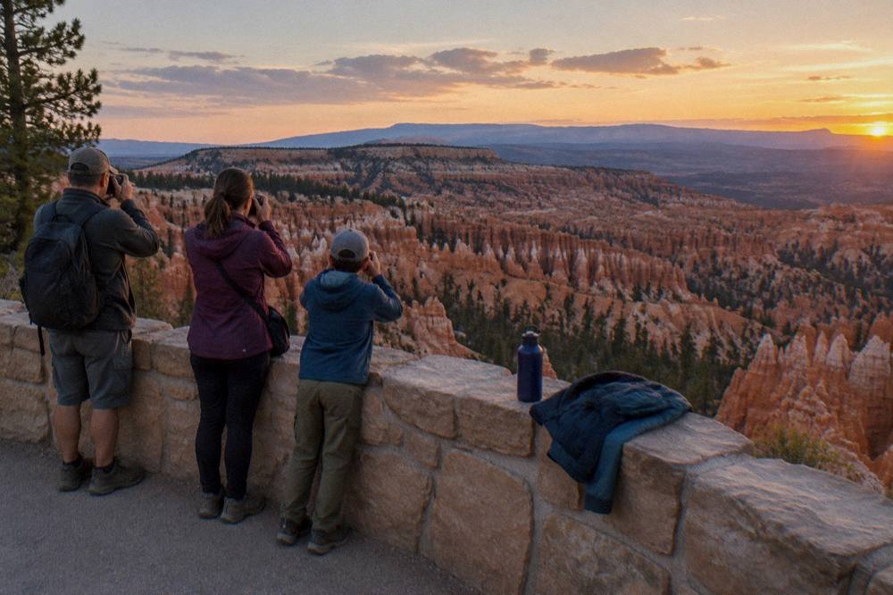 A family standing at a rim overlook photographing the hoodoo-filled amphitheater below