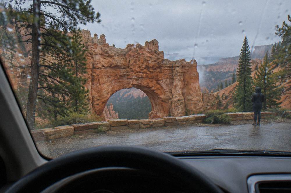 A steering-wheel view of a scenic overlook pullout sign beside red rock cliffs under a wide sky.