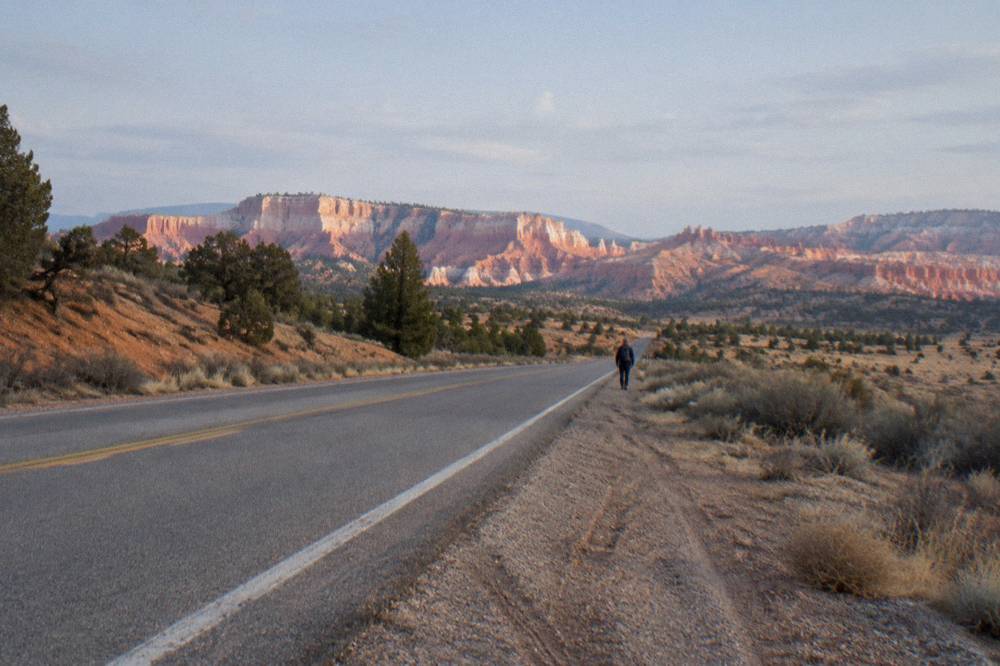 A desert highway heading toward distant plateaus under morning light.