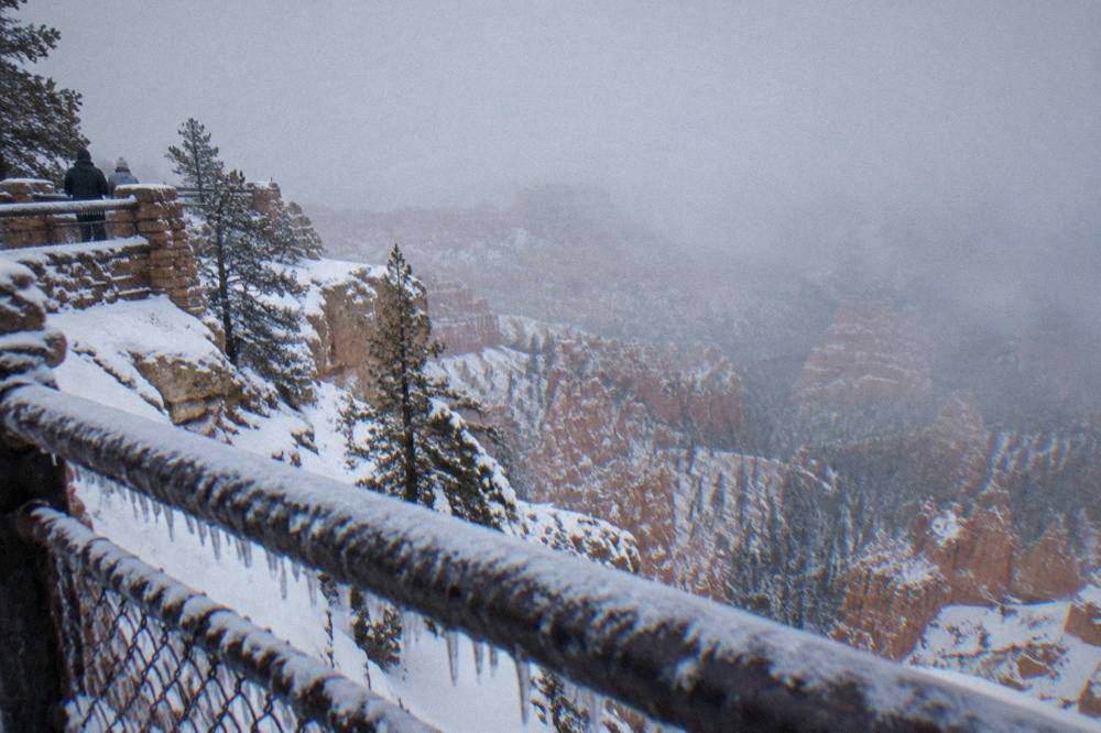 A snow-covered overlook railing above the frozen hoodoo formations of Bryce Amphitheater