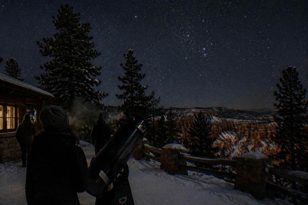 Telescopes and observers under a starry night sky above the snowy Bryce Canyon plateau