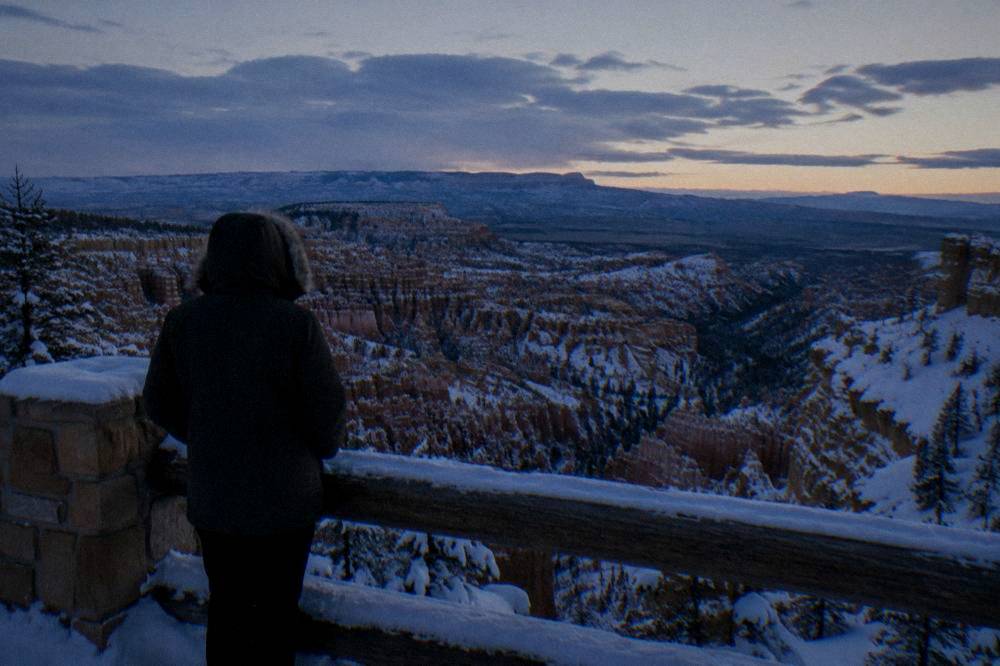 A lone visitor in winter clothing standing at a snowy overlook above Bryce Canyon