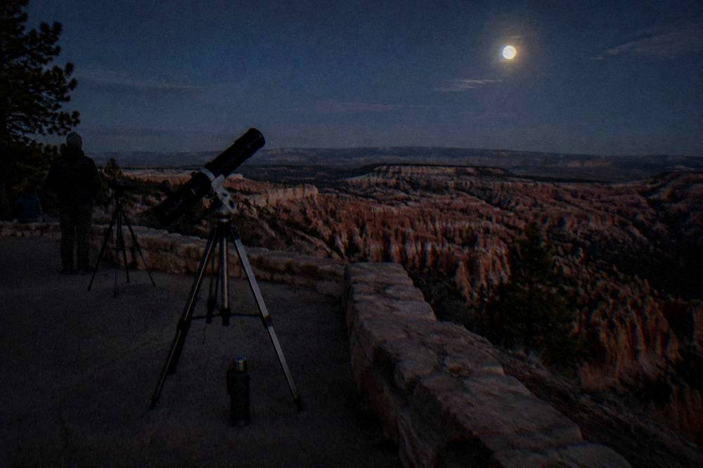 Telescopes set up on a rim viewpoint under a star-filled sky