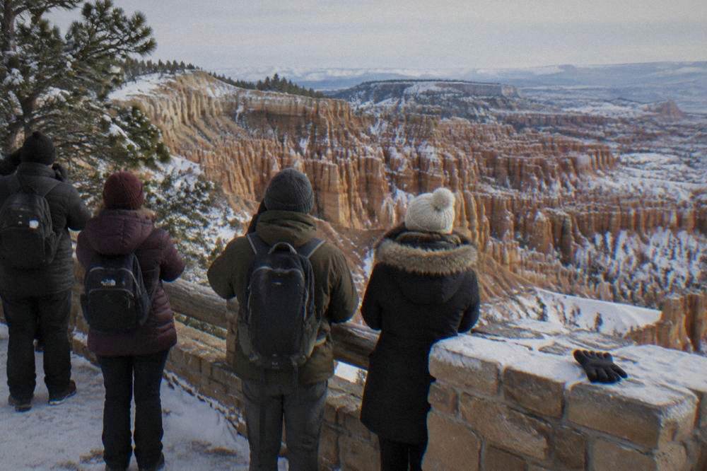 A guided tour group standing at a snow-dusted overlook above hoodoo formations