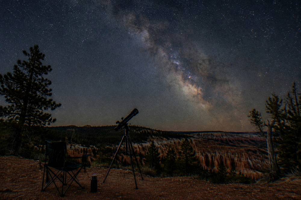 Telescopes silhouetted against a star-filled night sky above dark plateau horizon