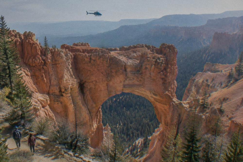 A helicopter flying above layered hoodoo formations and forest