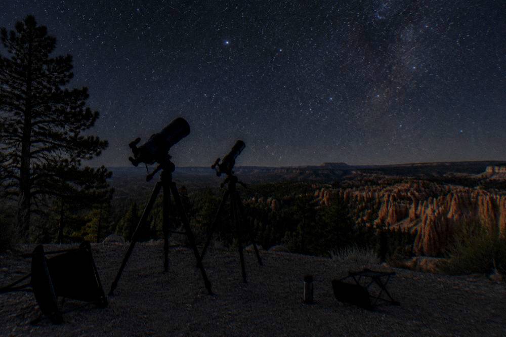 Telescopes silhouetted against a star-filled night sky above dark hills