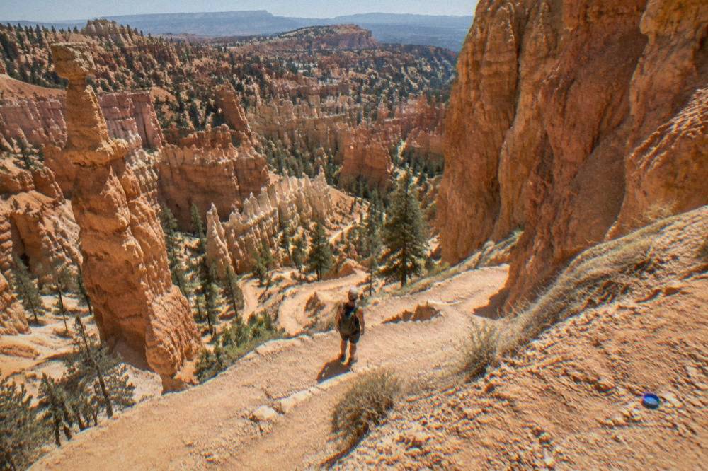 Hiker pausing on a switchback trail below towering hoodoo walls